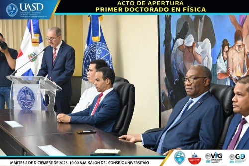 Fotografía del solemne acto de apertura del primer Doctorado en Física en la Universidad Autónoma de Santo Domingo (UASD). La imagen muestra la mesa de honor en el Salón del Consejo Universitario. De izquierda a derecha, se observa al Ministro de Educación Superior, Ciencia y Tecnología (MESCyT), de pie en el podio, dirigiéndose a la audiencia. Sentados en la mesa están el Director del Instituto de Física, con chacabana gris; el Decano de la Facultad de Ciencias, con traje y corbata azul oscuro; el señor Rector de la UASD, con traje y corbata azul claro; y el Vicerrector de Investigación y Postgrado, con traje y corbata morada. Detrás de ellos, se aprecian las banderas de la República Dominicana y de la UASD, y un mural artístico. En la parte superior de la imagen, un banner indica "ACTO DE APERTURA PRIMER DOCTORADO EN FÍSICA". En la parte inferior, se muestran los logos de la UASD, la Facultad de Ciencias, MESCyT, y las vicerrectorías correspondientes, junto con el texto "MARTES 2 DE DICIEMBRE DE 2025, 10:00 A.M. SALÓN DEL CONSEJO UNIVERSITARIO".